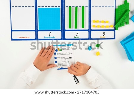 High-angle shot of a child's hands using colorful base ten blocks and a numerical mat to practice counting and understanding place values from ones to thousands.