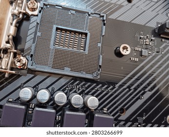 A high-angle shot of an empty LGA processor socket on a black computer motherboard, showing gold pins, capacitors, and intricate circuit board traces. Perfect for tech concepts, hardware upgrades, and IT repairs.