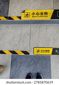 ​A high-angle shot looking down at stone tiled steps featuring yellow and black safety warning stickers that read 