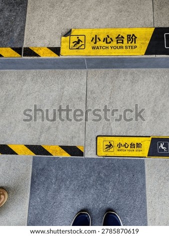 ​A high-angle shot looking down at stone tiled steps featuring yellow and black safety warning stickers that read 