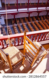 A high-angle shot looking down from the upper gallery, focusing on two foreground wicker chairs next to a red railing, with the lower patio seating visible below.
