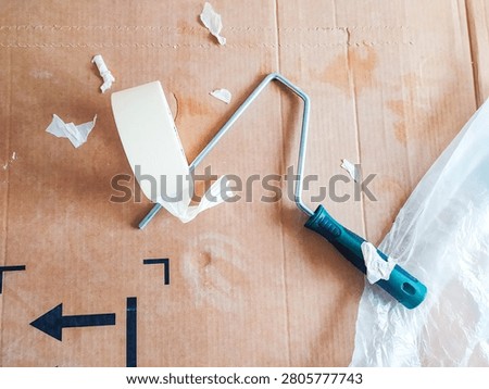 A highangle shot of a paint roller frame and masking tape on protective cardboard, capturing the messy, realistic process of DIY home improvement, renovation, and wall painting prep.