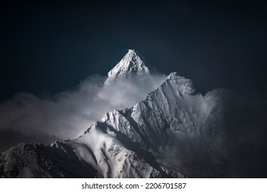 A high-angle shot of snowy mountains covered with clouds during a dark evening - Shutterstock ID 2206701587