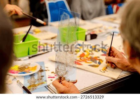 High-angle shot of a woman's hands using a stencil to paint motivational quotes and floral patterns on a canvas tote bag during a creative workshop