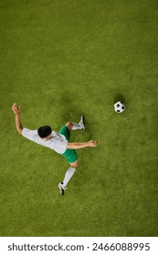 High-angle shot of young athletic man, football player poised to send soccer ball flying across vibrant green grass. Concept of professionals sport, competition, tournament, energy, action. Ad