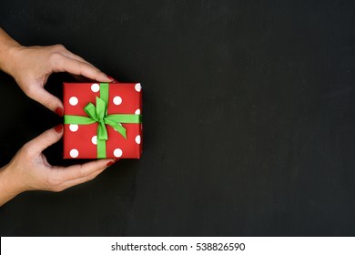 Happy Boxing Day Messages, Wishes, Quotes, And Images 48 high-angle shot of a young caucasian woman with a gift in her hands wrapped in a red paper patterned with white dots and tied with a green ribbon, on a dark gray surface