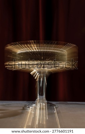 High-angle studio shot of a luxury fluted glass filled with sparkling wine or cocktail, standing on a reflective surface against a dramatic dark red curtain. The ribbed texture creates beautiful light distortions and a sophisticated aesthetic.