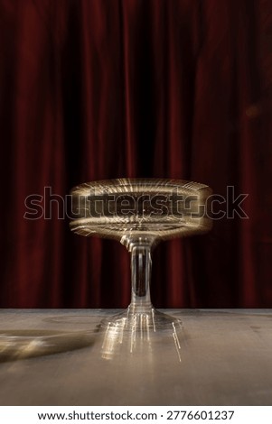 High-angle studio shot of a luxury fluted glass filled with sparkling wine or cocktail, standing on a reflective surface against a dramatic dark red curtain. The ribbed texture creates beautiful light distortions and a sophisticated aesthetic.