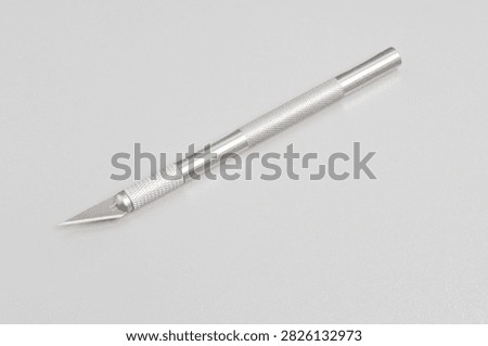 High-angle studio shot of a precision craft knife with a sharp metal blade and textured aluminum handle. Placed diagonally on a clean light grey background. Ideal for design, DIY crafting, art supplies, and hobby concept visual content.