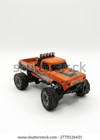 A high-angle studio shot of a weathered orange toy monster truck. The miniature pickup features 