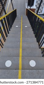 	A high-angle, symmetrical shot looking down a set of concrete stairs at a railway or train station. The image features clear, circular white safety markings on the steps.