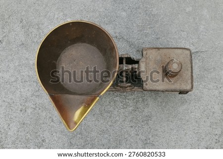 A high-angle, top-down shot of a vintage rusty iron balance scale with a large copper weighing pan and a metal weight, sitting on a concrete surface.