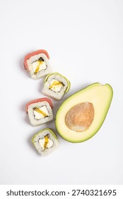 A high-angle, top-down studio shot against a seamless white background featuring four pieces of fusion sushi rolls and a fresh avocado half with the pit still intact.