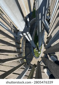 High-angle, top-down view of a modern spiral wooden and metal staircase structure with strong geometric shadows on a sunny day.