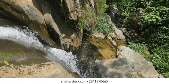 A high-angle vertical shot looking down from the top of a tropical waterfall, capturing white water rushing over the edge next to a steep, rocky cliff with lush greenery in Binh An, Tuyen Quang, Vietnam.