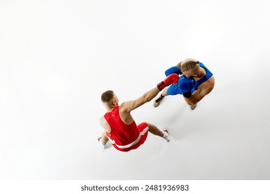 High-angle view of boxing match, capturing moment punch thrown by boxer in red towards blue-clad competitor against white studio background. Concept of professional combat sport, competition. Ad
