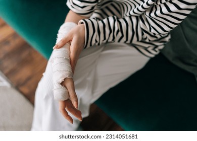 High-angle view cropped shot of unrecognizable young woman with broken right hand wrapped in white gypsum bandage, gently massaging injured wrist. Unhappy female with broken arm from accident at home. - Powered by Shutterstock