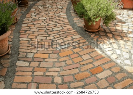 High-angle view of a curving stone pathway in a garden setting. Terracotta pots filled with lavender plants flank the path, adding a touch of natural beauty