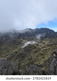 High-angle view of a dramatic volcanic crater valley surrounded by rugged mountain ridges and mist
