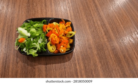 A high-angle view of fresh culinary condiments featuring sliced red and orange bird's eye chilies alongside chopped green scallions. These organic ingredients are neatly presented in a black divided dipping dish on a dark wooden textured surface, perfect for adding spicy flavor to Asian cuisine.