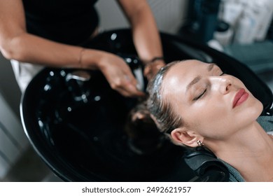 High-angle view of hairdresser washing head of young woman in beauty hairdressing salon. Close-up of unrecognizable hairstylist foaming shampoo on long blonde hair of beautiful female client. - Powered by Shutterstock