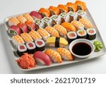 A high-angle view of a large platter filled with various types of sushi and sashimi, including tuna, shrimp, salmon, and california rolls, with wasabi and pickled ginger, on a white background.