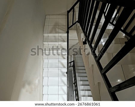 High-angle view looking down a multi-level indoor staircase with white tiled steps and landings, featuring a black metal railing