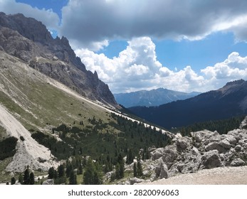 A high-angle view looking down over dark green alpine forests and soaring mountain peaks surrounded by low clouds in the Vajolet area of Alto Adige, Italy.