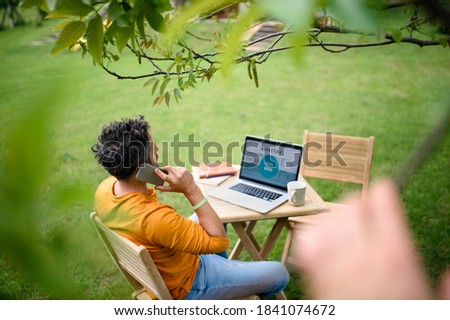 High-angle view of man with laptop and smartphone working outdoors in garden, home office concept.