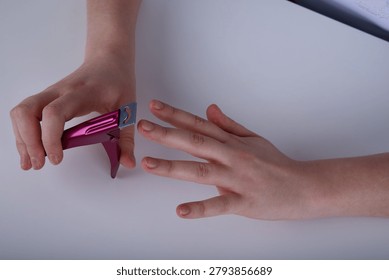 High-angle view of a person using a pink metallic acrylic nail tip clipper cutter tool on fingernails..jpg
