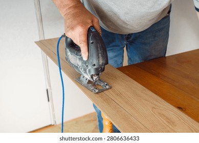 A high-angle view of a professional carpenter using an electric jigsaw to cut a laminate plank precisely along a drawn pencil line during flooring installation.