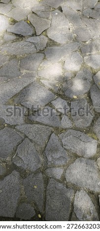High-angle view of a rustic grey crazy paving stone floor texture with natural sunlight and shadows, ideal for architectural and garden design backgrounds.
