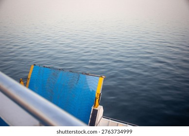 High-angle view from a ship deck showing a blue metal loading ramp and the vast expanse of the sea. Minimalist maritime concept representing travel, transportation, and journey