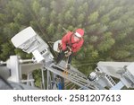 A high-angle view of a telecommunications technician working at height on a telecom tower, performing maintenance on communication equipment. 