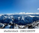 A high-angle view of the top of Cerro Catedral, a snowy mountain in a ski resort in Argentina with a blue lake and a blue sky with clouds in the background.
