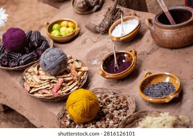 High-angle view of a traditional textile workshop table in Peru, filled with ceramic bowls of natural mineral fixatives, cochineal powder, and baskets of wool yarn balls.