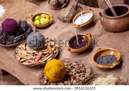 High-angle view of a traditional textile workshop table in Peru, filled with ceramic bowls of natural mineral fixatives, cochineal powder, and baskets of wool yarn balls.