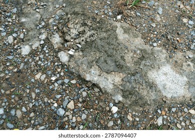 High-angle view of a weathered ground surface featuring cracked concrete covered in moss, surrounded by loose gravel and dirt.
