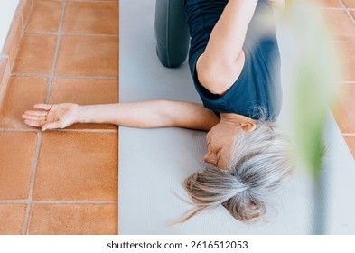 High-angle view of woman practicing Thread the Needle pose with one arm extended the floor