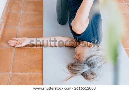 High-angle view of woman practicing Thread the Needle pose with one arm extended the floor