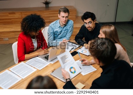 High-angle view of young startup businesspeople discuss corporation project planning sit at meeting table in boardroom. Company managers brainstorm financial plan working together with document papers