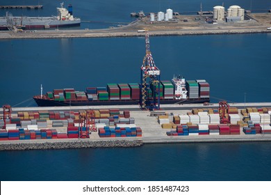 High-angle wide shot of the side view of a container ship anchored at a commercial harbor.