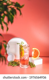 Highball glass of fresh grapefruit cocktail with ice, rosemary and thyme on pink table surface, spring summer art drink food concept.