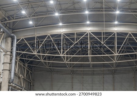 High-ceilinged interior with metal beam grid, artificial diffused lighting, empty foreground, geometric patterns, smooth reflective floor