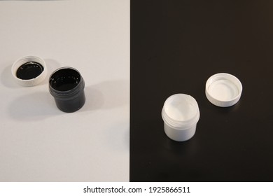 High-contrast Close-up Image.Black Paint Jar With Open Lid On White Light Container On Black.Conceptual Photography Of Opposites