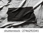High-contrast composition featuring a jagged, rectangular scrap of black paper centered on a heavily creased and weathered white paper surface.