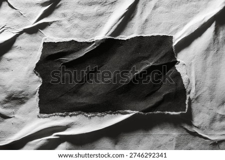 High-contrast composition featuring a jagged, rectangular scrap of black paper centered on a heavily creased and weathered white paper surface.