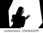 High-contrast silhouette of a woman in a graceful pose against a white background. The backlight highlights her elegant form, creating an abstract, artistic, and expressive image