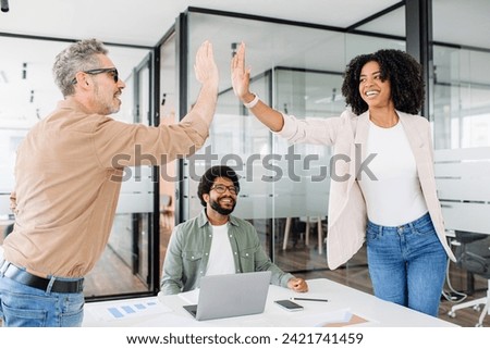 A high-five gesture between colleagues in a modern office space highlights a successful moment, with the surrounding team sharing in the jubilant spirit, a celebratory work environment