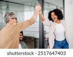 A high-five moment captures the joyful success within a team, as a woman beams with pride and a colleague applauds, showcasing a supportive and uplifting office culture. Value of team achievements